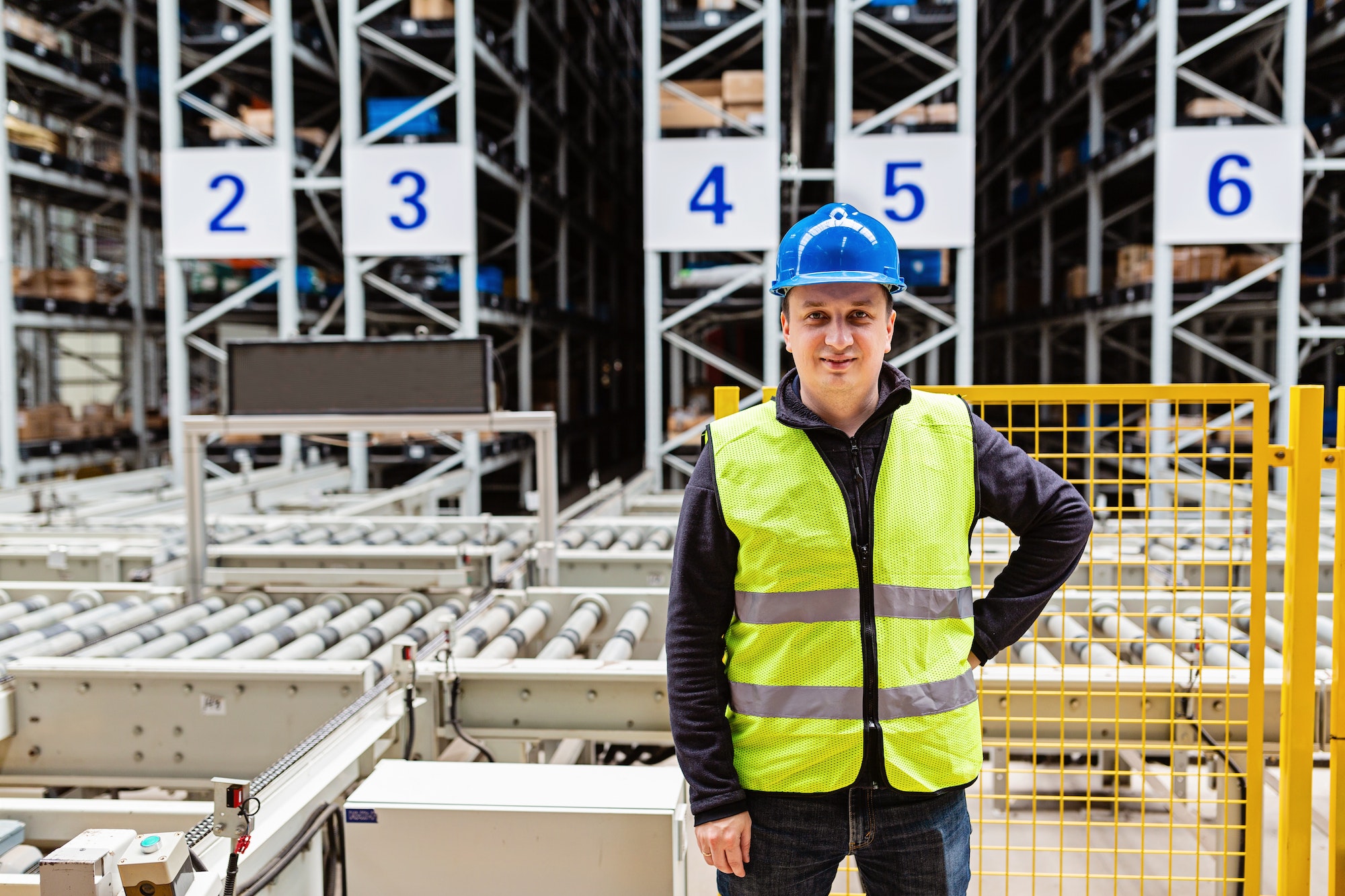 Factory employee is posing in helmet. Caucasian man 30 years old works in automatic warehouse